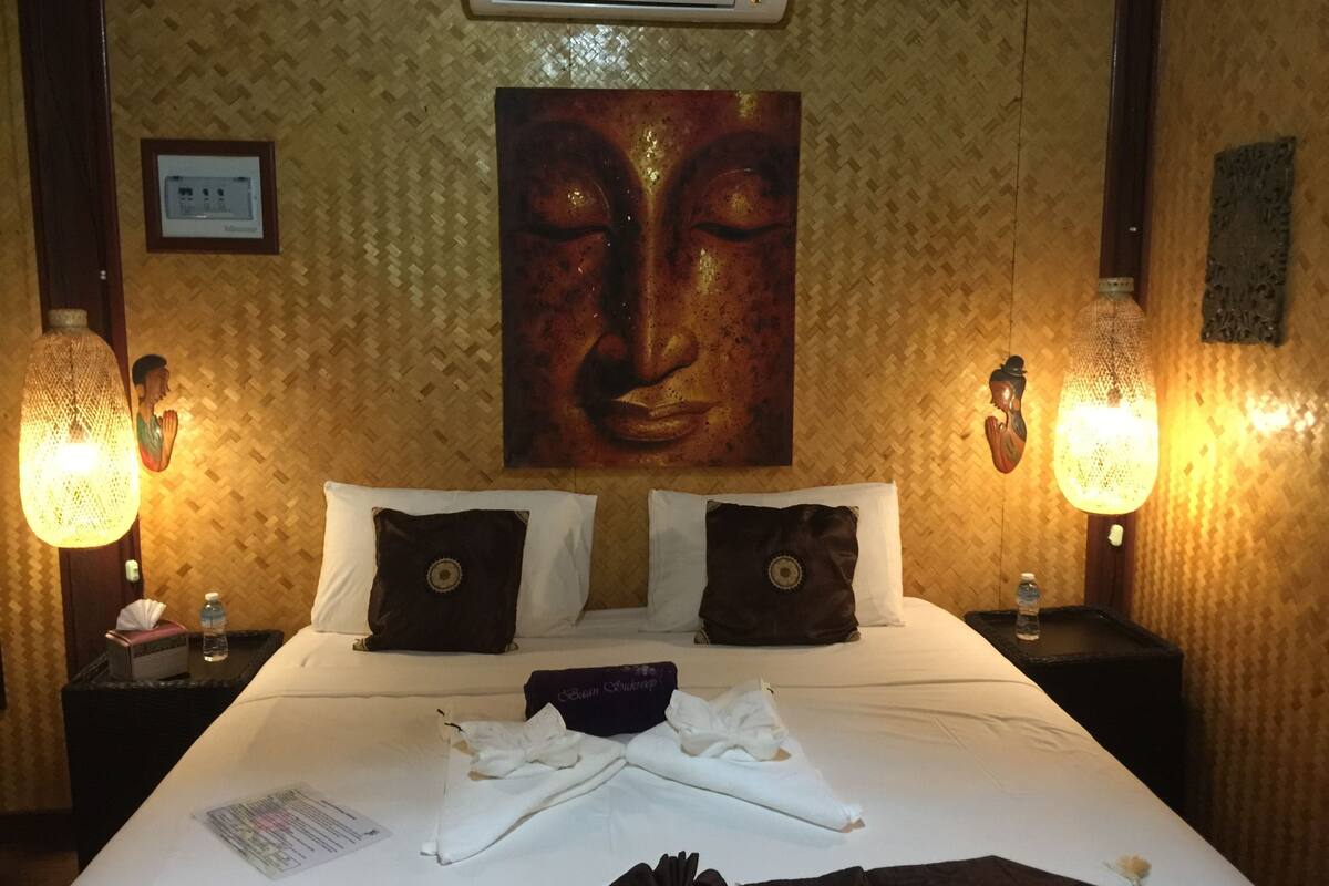A hotel room with a large bed, two nightstands, a wall-mounted air conditioner, and a painting above the bed.