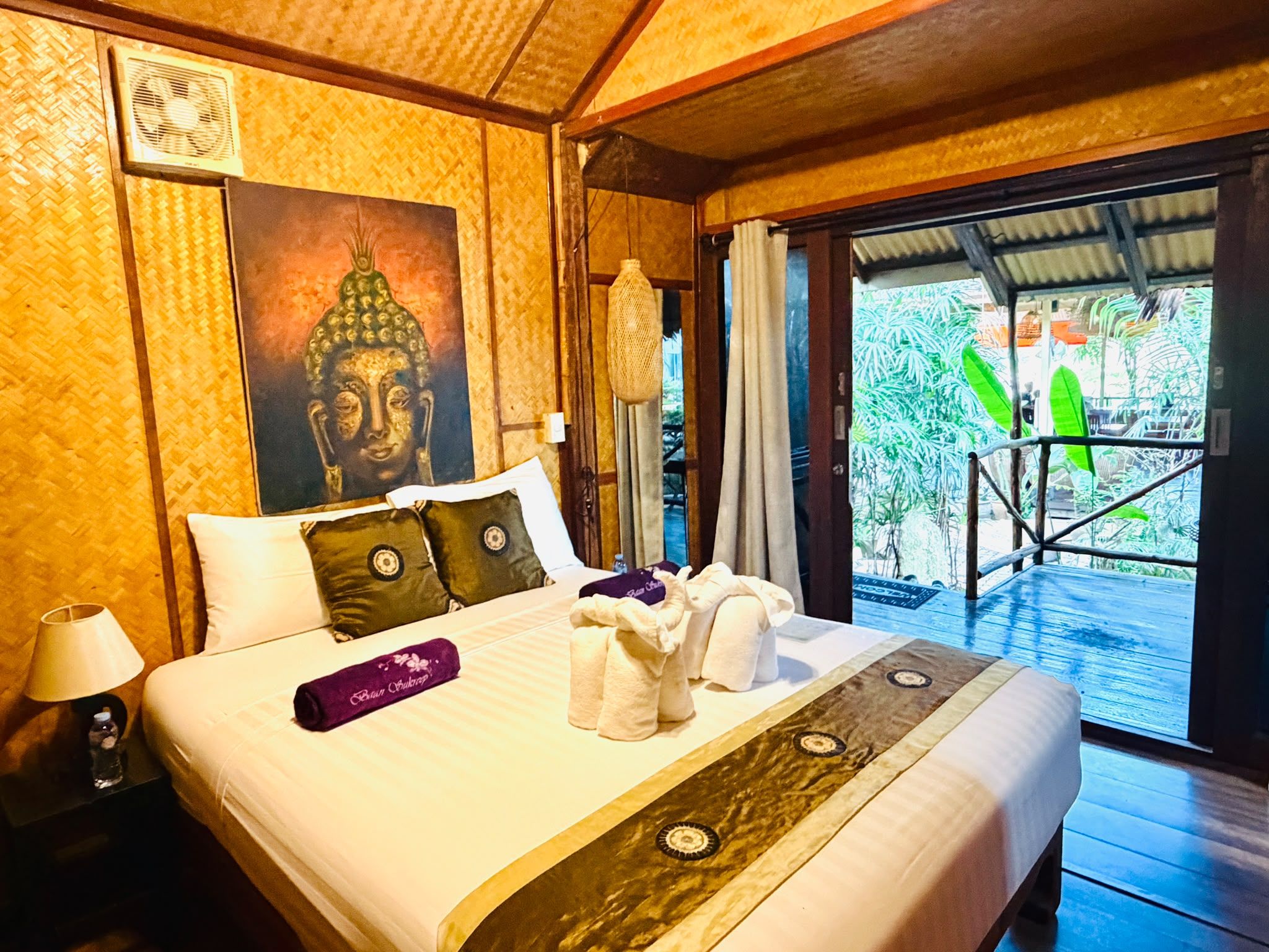 Une chambre d’hôtel avec un lit, des oreillers, un tableau, une lampe et une vue sur la verdure.