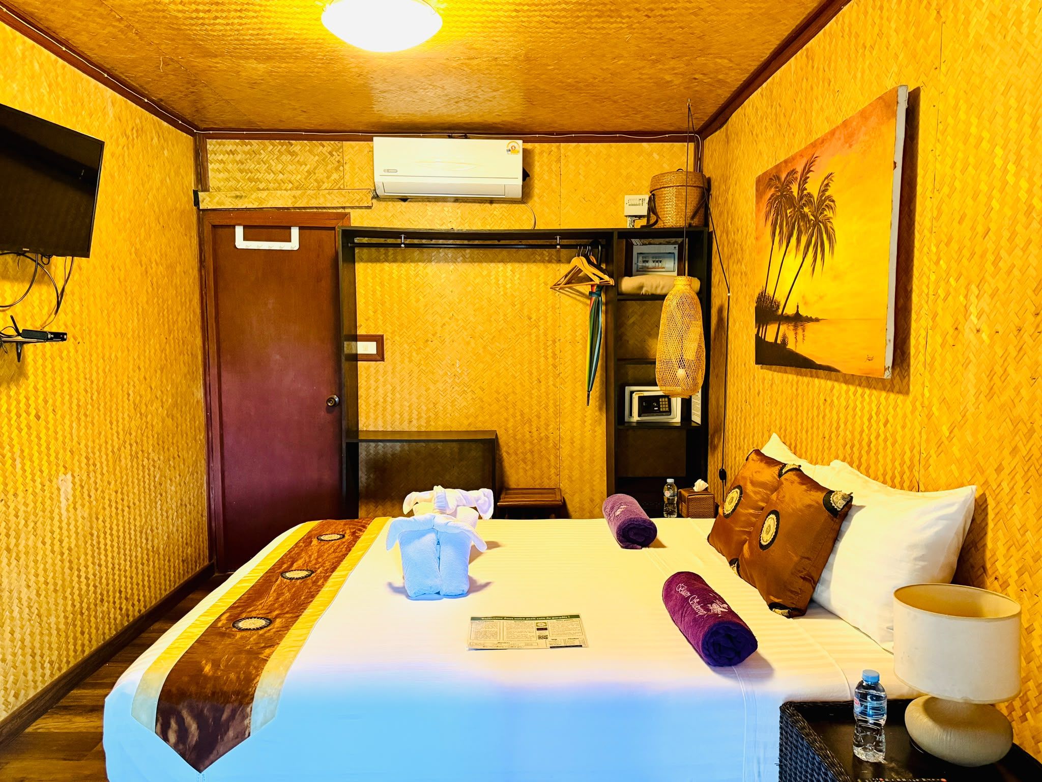 Une chambre d’hôtel comprenant un lit, un téléviseur à écran plat, un appareil de climatisation, un tableau et une porte donnant accès à une salle de bain.