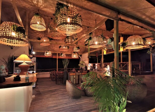 Un restaurante con terraza de madera, lámparas de mimbre colgantes y una zona de bar.