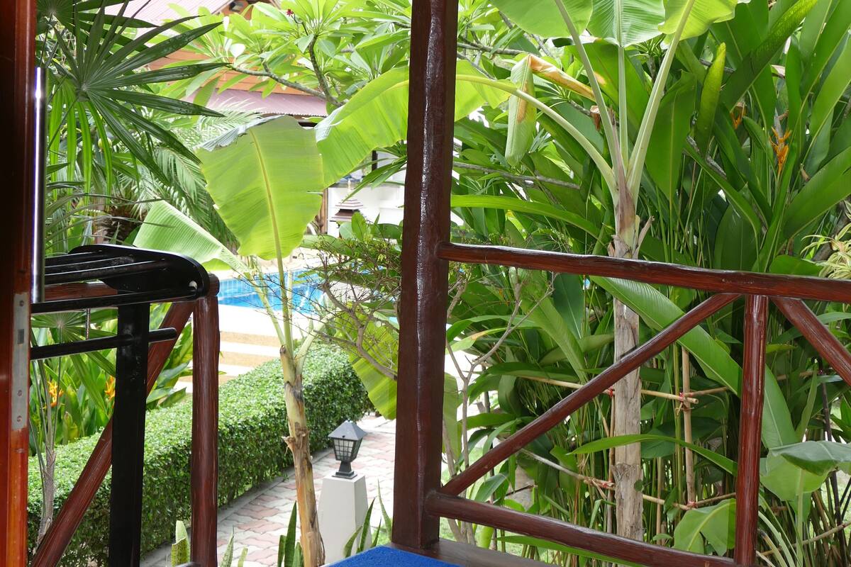 A wooden deck with a blue mat, surrounded by lush tropical plants and a corrugated metal roof.