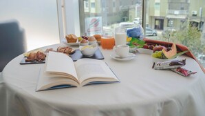 Une table de petit-déjeuner avec un livre, des œufs, du jus, du lait, des viennoiseries et des fruits.