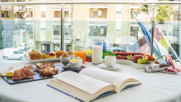 Une table de petit-déjeuner avec de la nourriture, un livre et une vue sur des bâtiments.