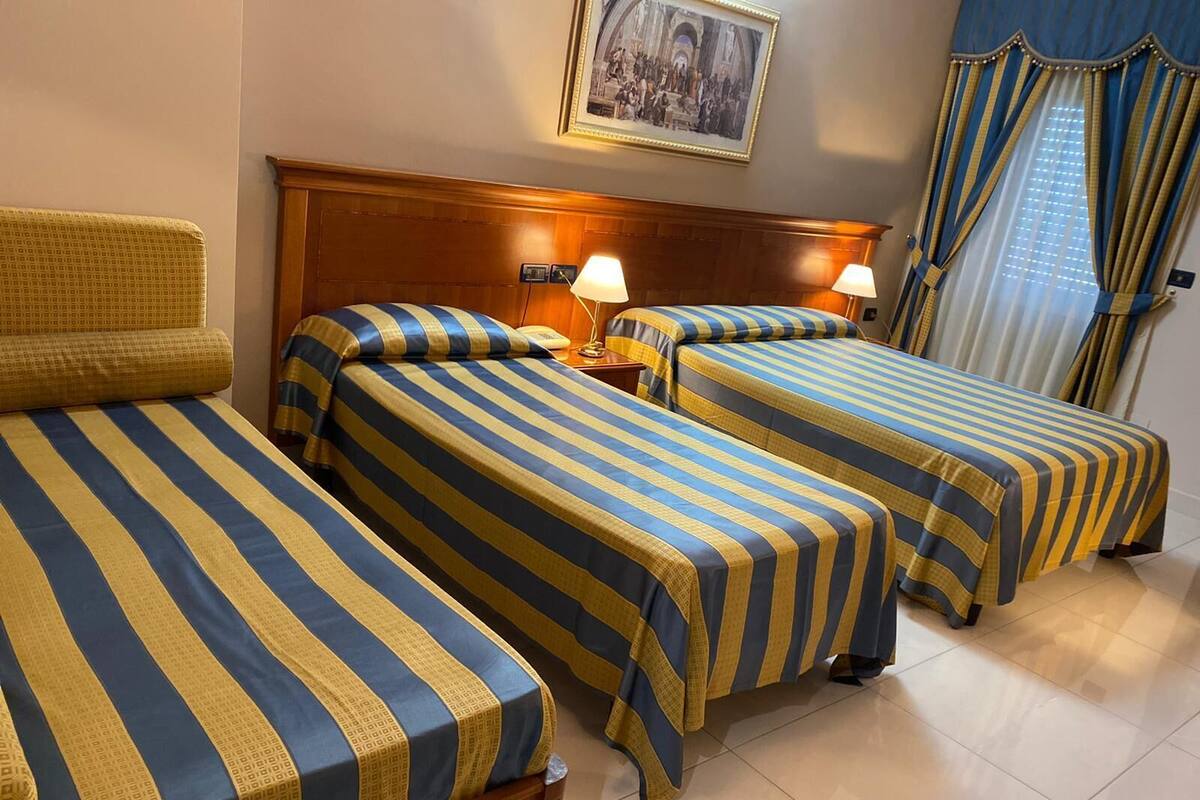 A hotel room with two single beds, a wooden headboard, bedside lamps, and a framed picture on the wall.