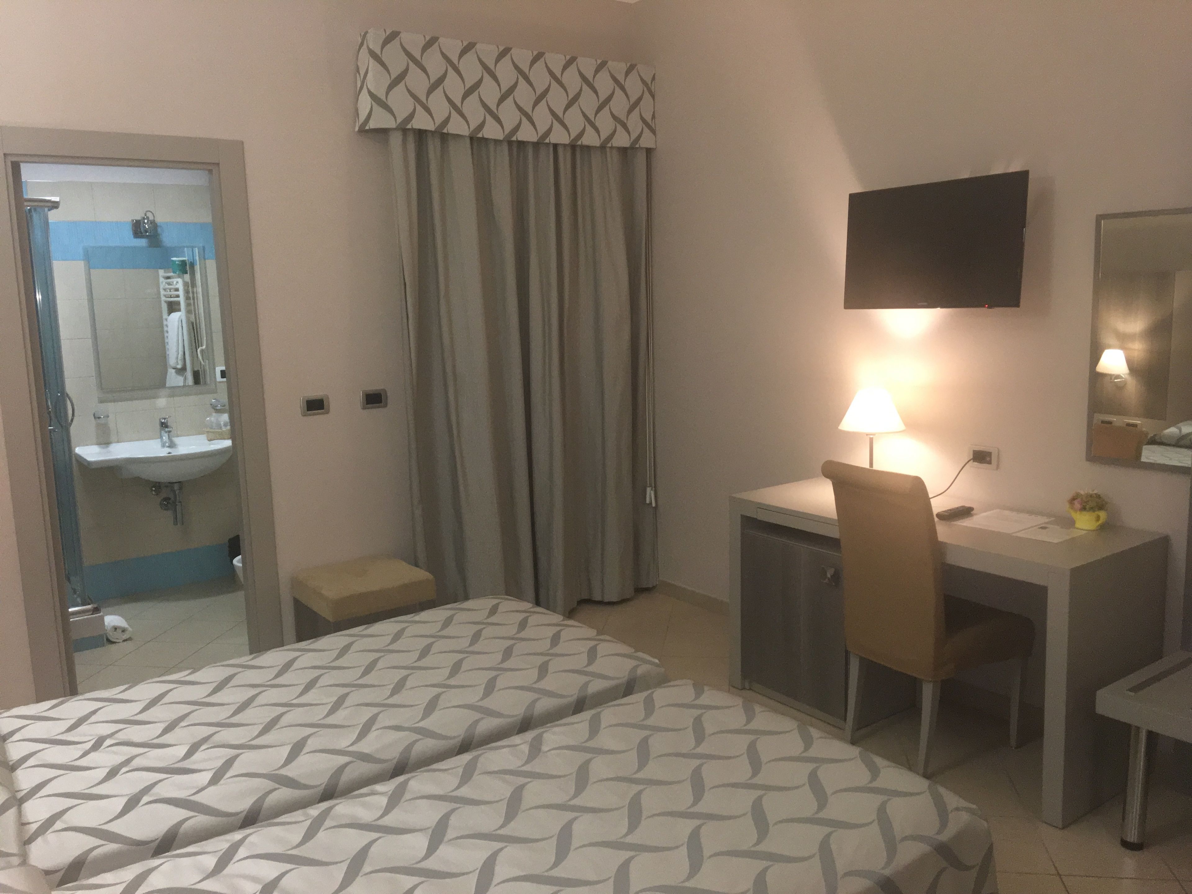 Una camera d'albergo con un letto, una scrivania, una sedia e una televisione.