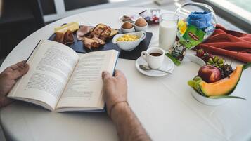 Una persona leyendo un libro en una mesa con alimentos para el desayuno, como tostadas, huevos, leche, café y fruta.