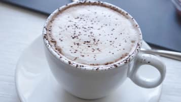 A cup of coffee with a frothy top, a spoon, and a pastry on a table.