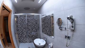 Een moderne badkamer met een douchekabinet van glas, een witte wastafel en een aan de muur bevestigde haardroger.