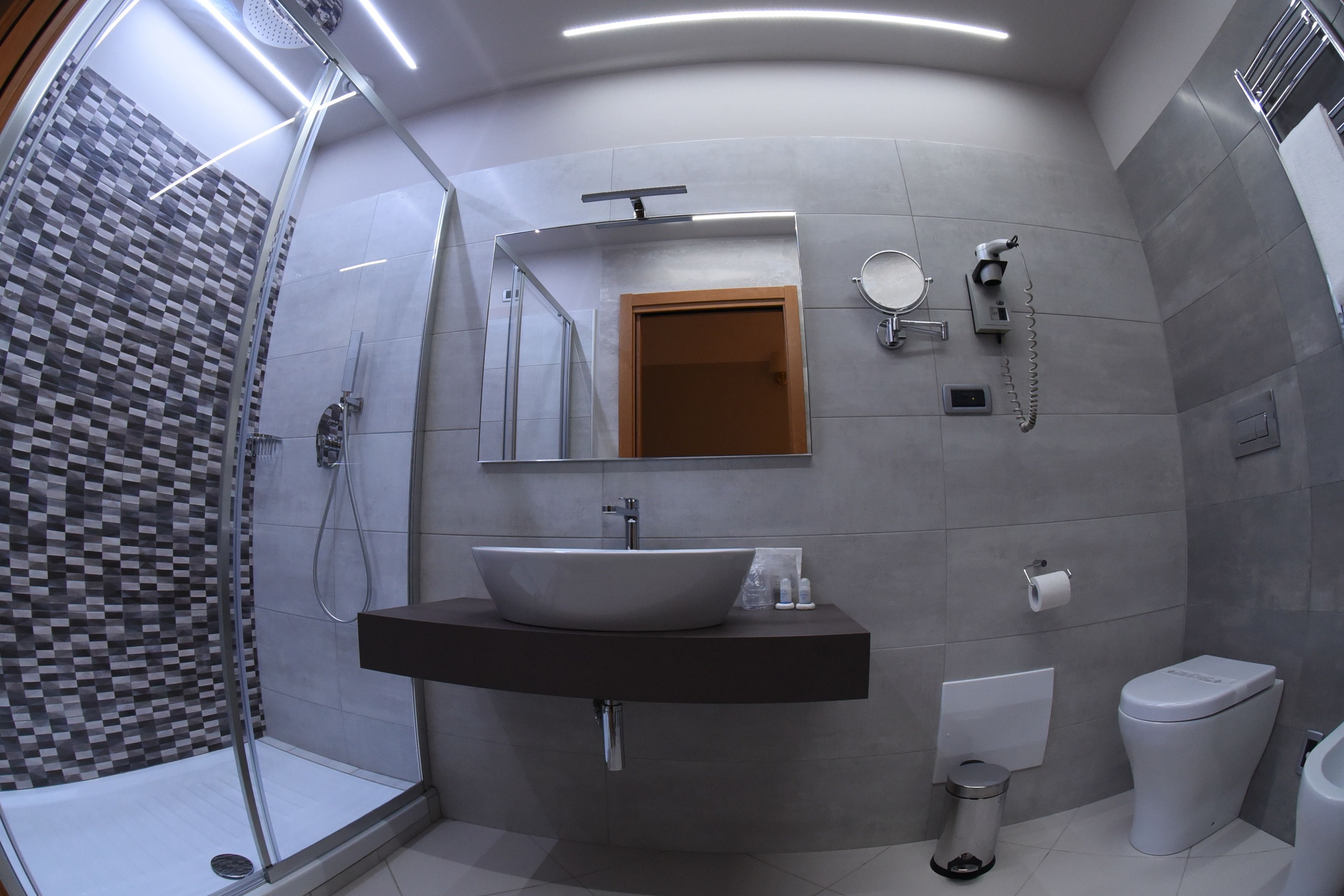 Un bagno moderno con un lavandino capiente, uno specchio, un water e una zona doccia.