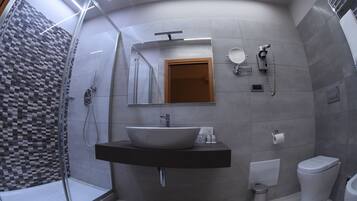 Un bagno moderno con un lavandino capiente, uno specchio, un water e una zona doccia.