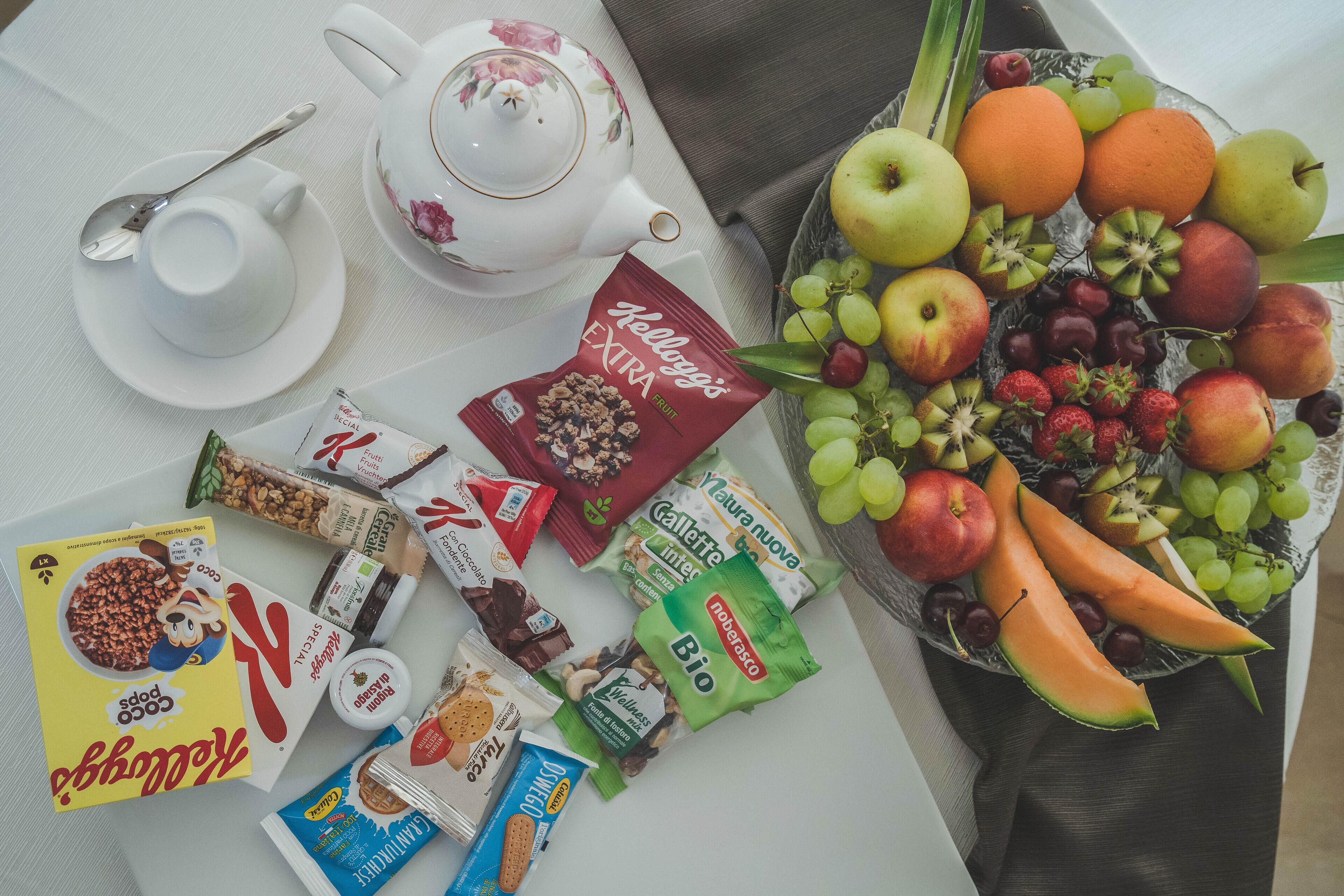 Mesa de desayuno con frutero, juego de té y diversos snacks envasados.