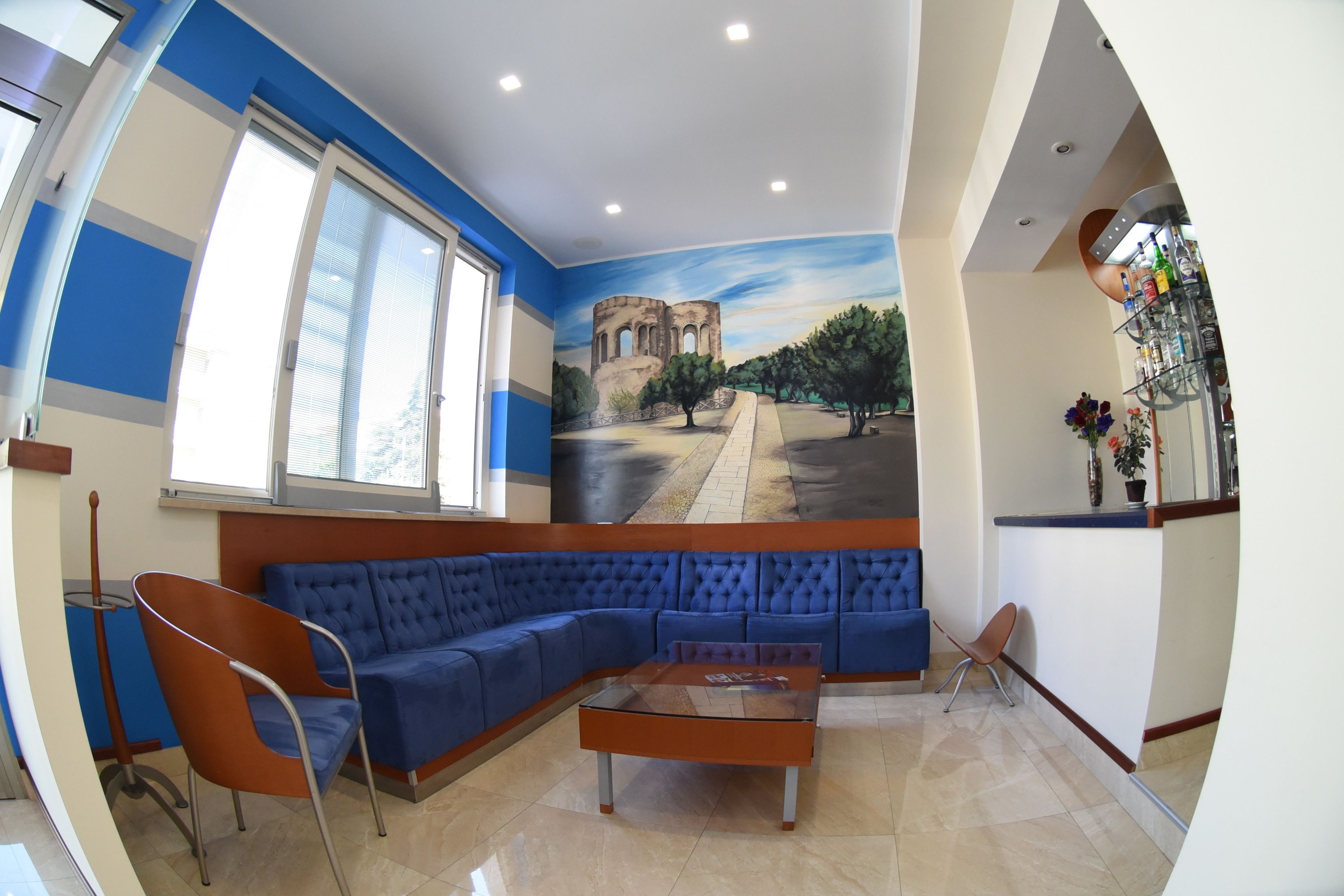 A modern waiting area with a blue sectional sofa, a glass coffee table, and a mural of a historical building.