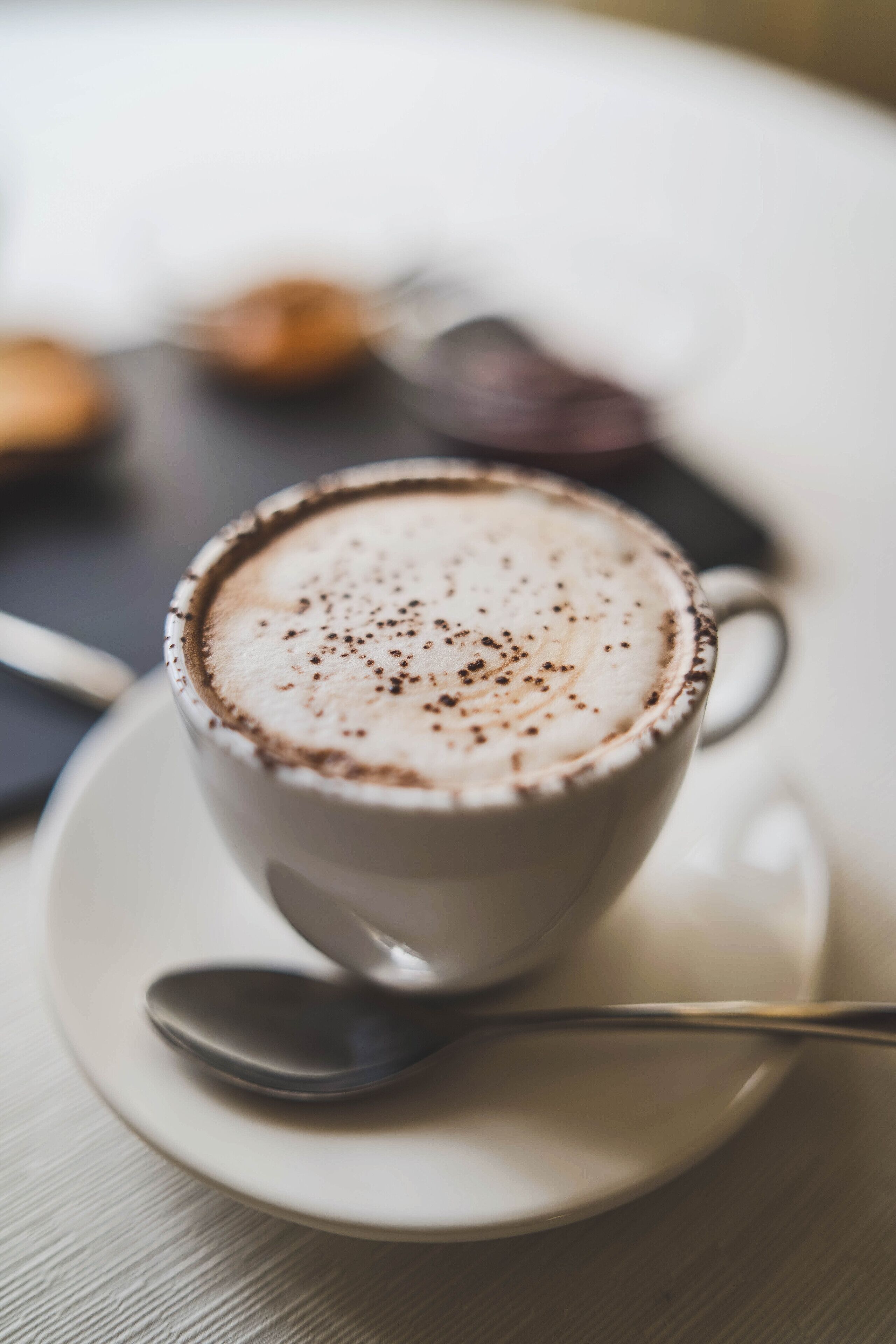 Una taza de café con espuma, sobre un plato y una cuchara al lado.