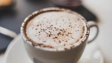 Una taza de café con espuma, sobre un plato y una cuchara al lado.