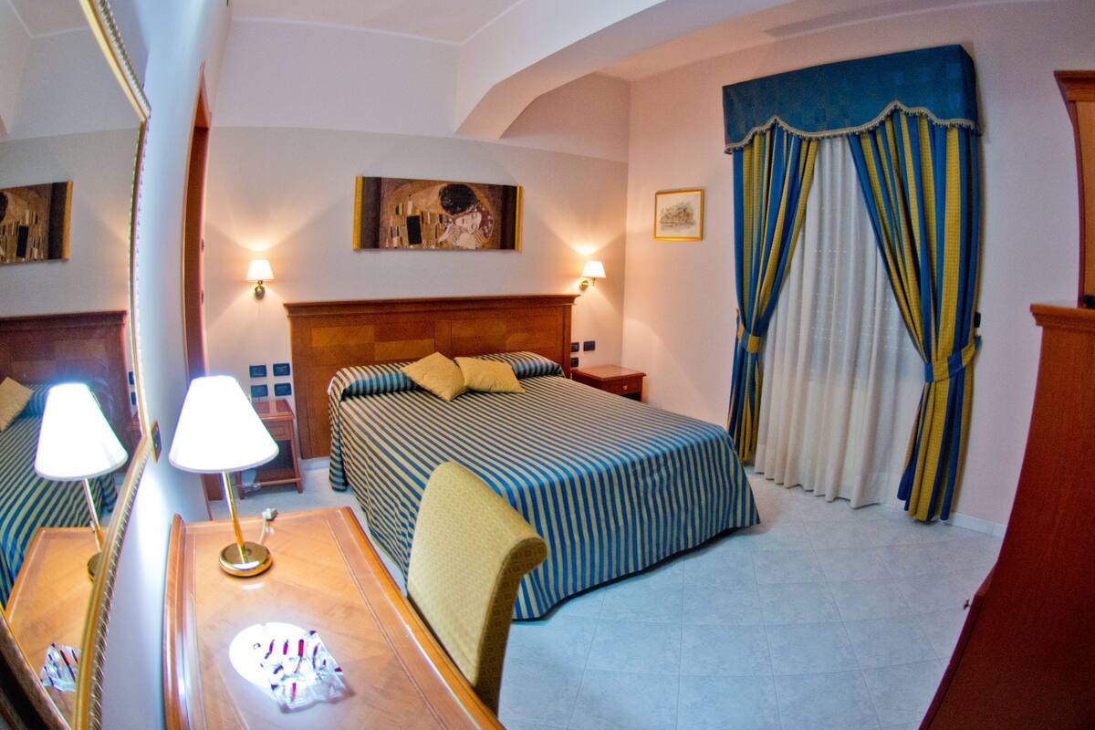 A hotel room with a bed, bedside tables, lamps, a desk, and a chair.