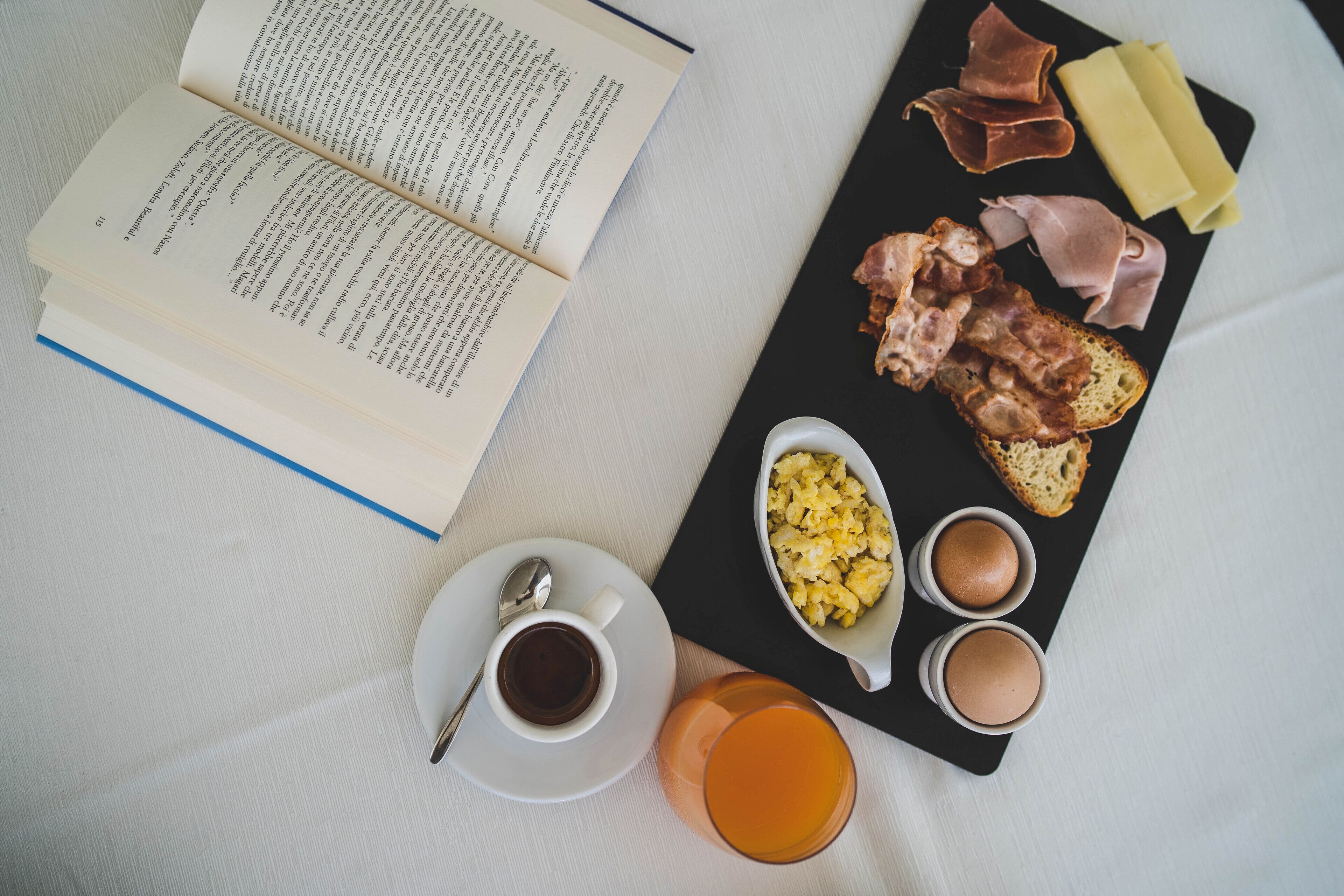 A book, a black tray with food items, and a cup of tea on a table.