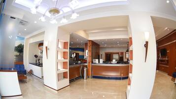 A modern hotel lobby with a reception desk, seating area, and a chandelier.