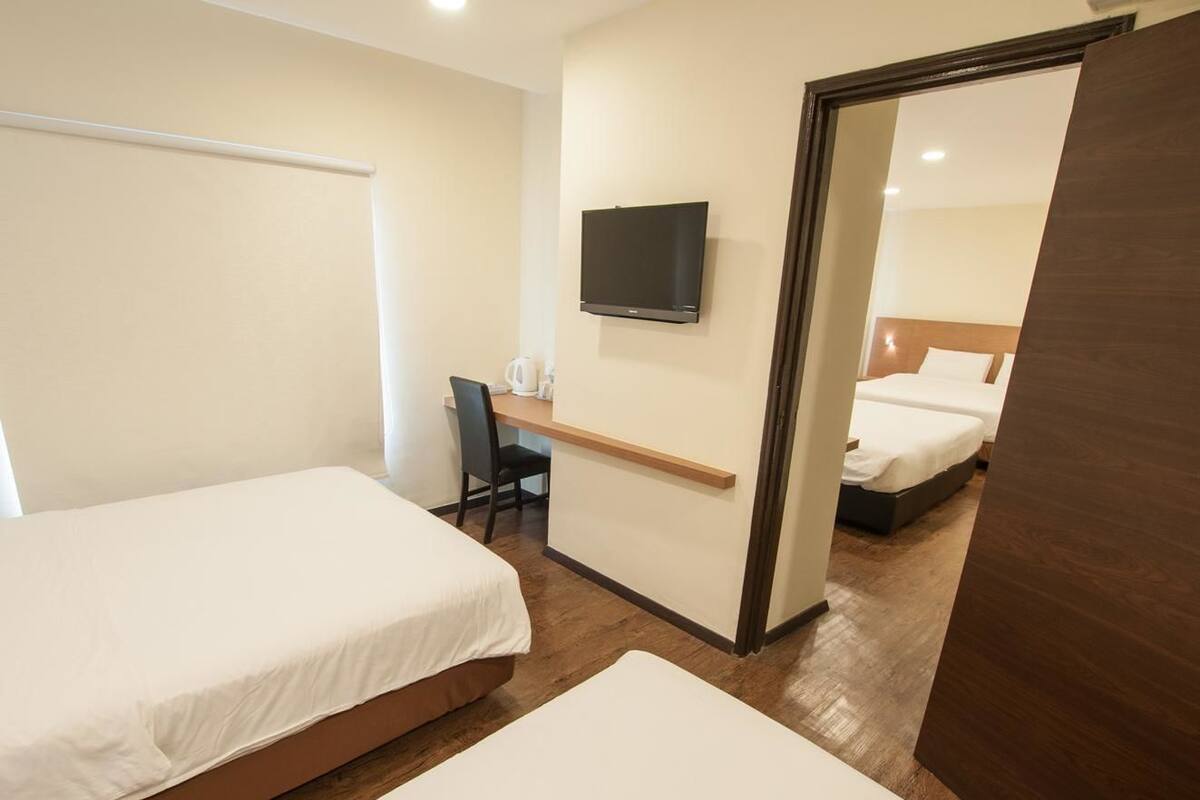 Quarto de hotel com duas camas, uma escrivaninha, uma cadeira, uma televisão e um espelho.