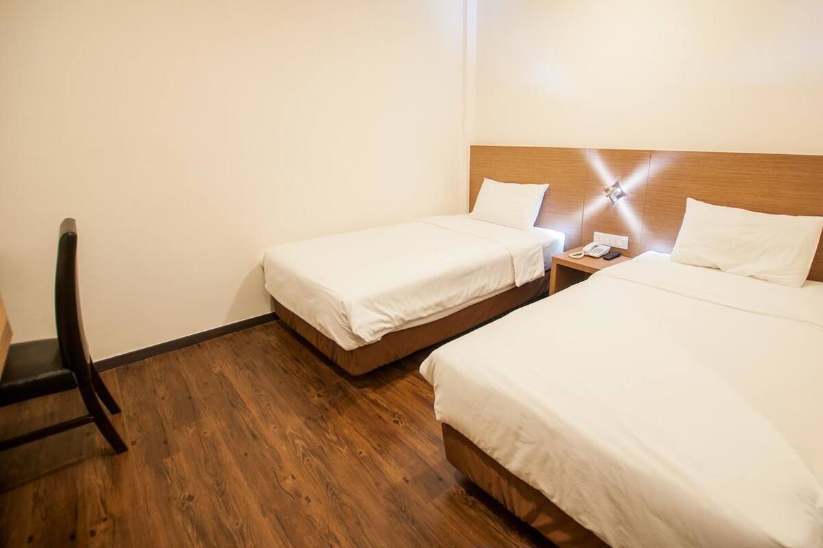 Quarto de hotel com duas camas de solteiro, piso de madeira, mesa de cabeceira com telefone e uma cadeira.