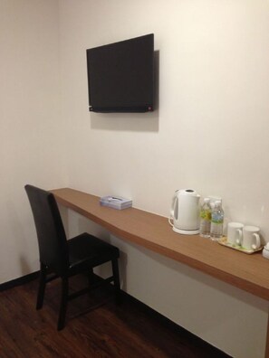 A small room with a wooden desk, a black chair, a flat-screen TV mounted on the wall, and a kettle on the desk. - Nagoya Inn Hotel (Langkawi)
