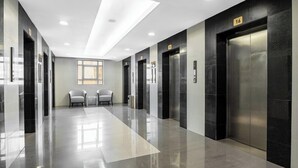 A modern elevator lobby with a reflective floor, two chairs, and a large window. - Elaf Bakkah Hotel (Makkah)