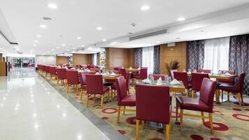 Un vaste espace de restauration d’hôtel, avec des chaises et des tables rouges, un sol ciré et un design moderne au plafond.