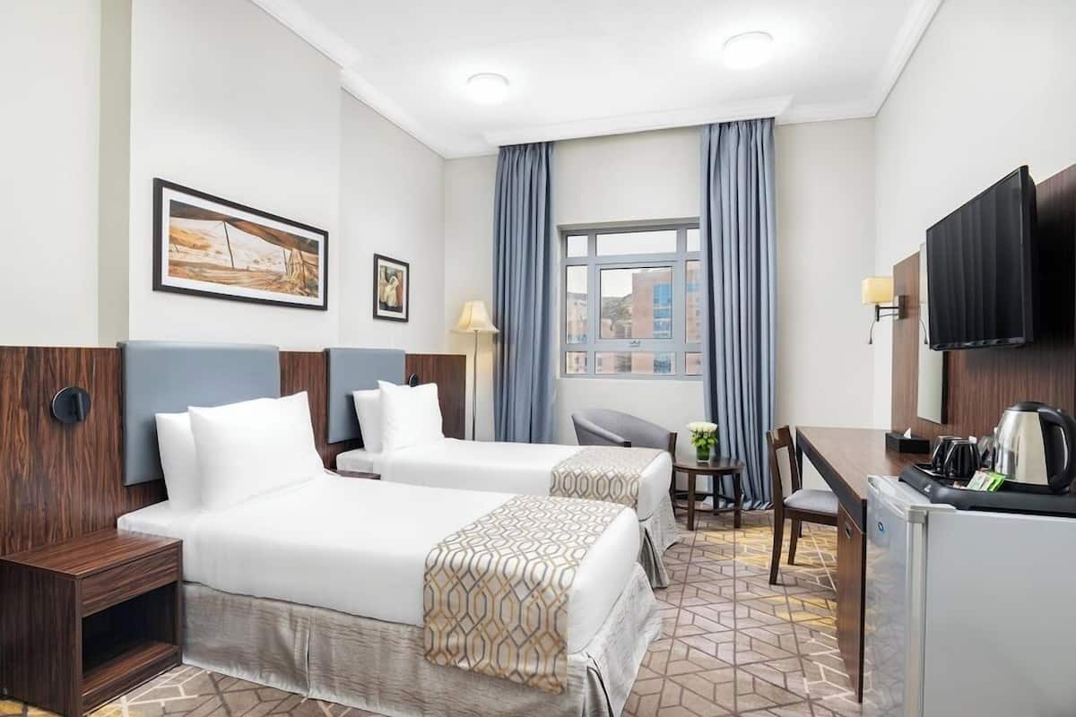 Ein Hotelzimmer mit zwei Betten, einem Schreibtisch, einem Stuhl, einem Fernseher und einem Fenster mit Vorhängen.
