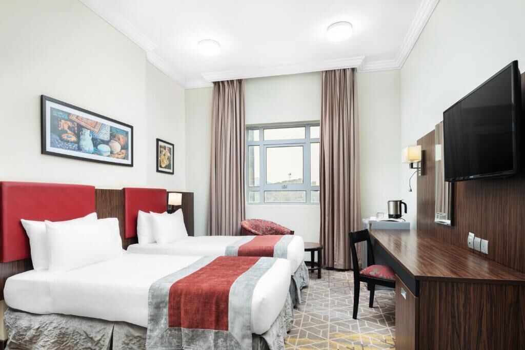 A hotel room with two beds, a desk, a television, and a window with curtains.