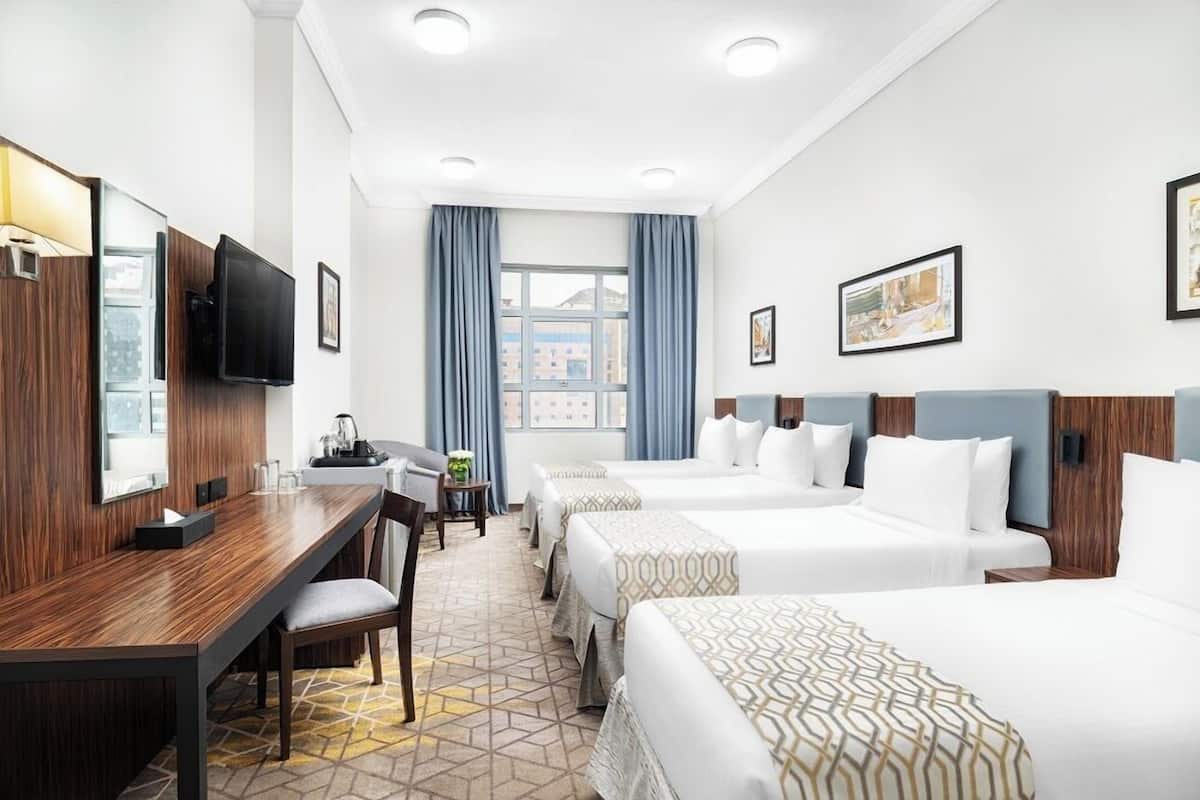 Ein Hotelzimmer mit zwei Betten, einem Schreibtisch, einem Sessel, einem Fernseher und einem Fenster mit Vorhängen.