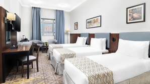A hotel room with two beds, a desk with a TV, and a window with curtains. - Elaf Bakkah Hotel (Makkah)