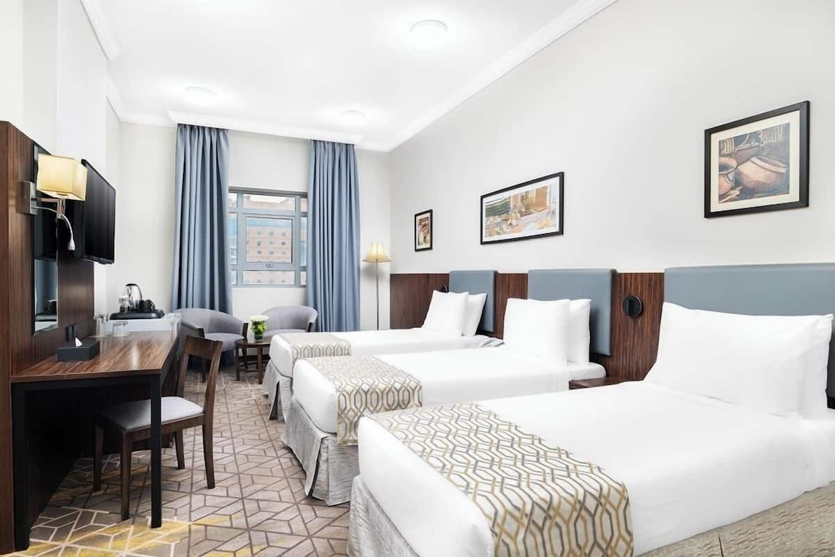 Ein Hotelzimmer mit zwei Betten, einem Schreibtisch mit Fernseher und einem Fenster mit Vorhängen.