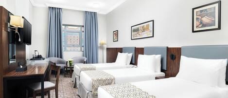 Ein Hotelzimmer mit zwei Betten, einem Schreibtisch mit Fernseher und einem Fenster mit Vorhängen.