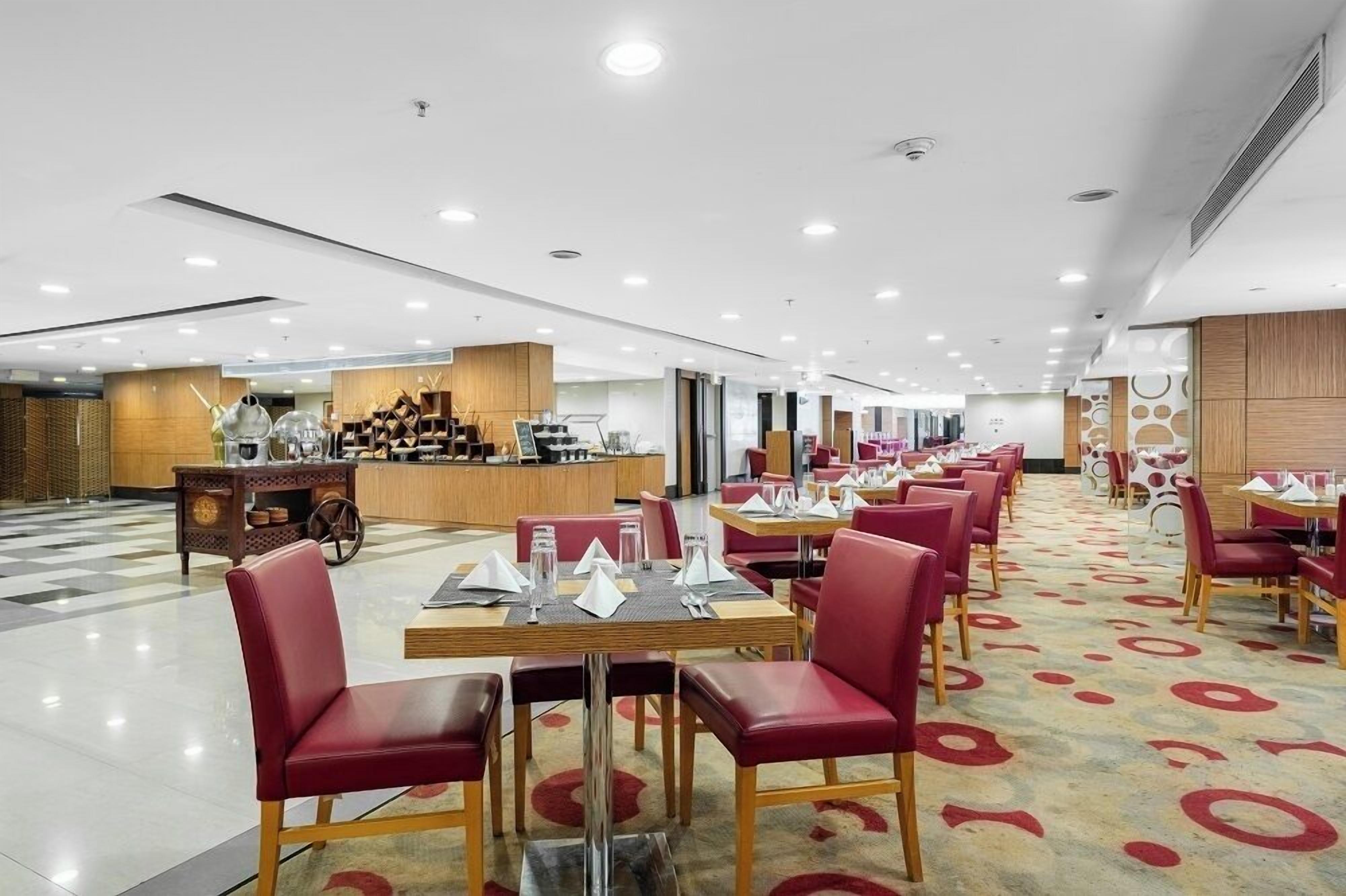 Un vaste espace de restauration dans l’hôtel, avec de nombreuses tables et chaises, un comptoir de réception et un guichet d’enregistrement.