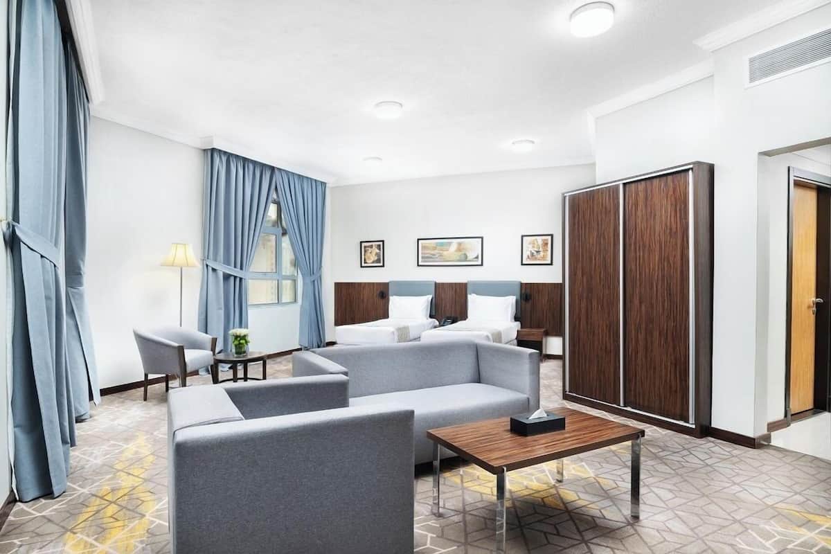 Ein Hotelzimmer mit einer Couch, einem kleinen Tisch, einem Bett mit zwei Kissen, einem Kleiderschrank und einem Fenster mit Vorhängen.