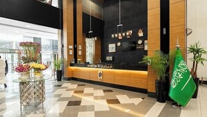 A reception area with a black and wood panel design, a reception desk, and a green flag with Arabic script. - Elaf Bakkah Hotel (Makkah)