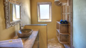 A bathroom with a stone sink, a mirror with an ornate frame, a small window, and a shelf with bottles. - Les Villas Ottalia Gili Trawangan (Gili Trawangan)