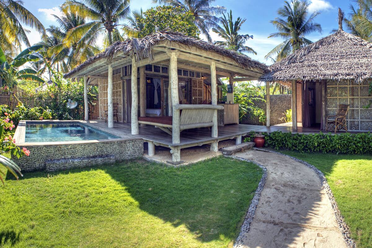 A tropical resort with a pool, a thatched-roof gazebo, and lush greenery.