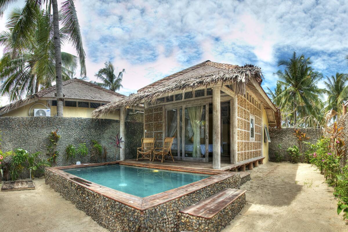 A resort with a pool, thatched-roof structures, and tropical vegetation.
