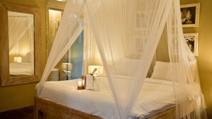 A bed with a canopy, a bedside table with a lamp, and framed pictures on the wall. - Les Villas Ottalia Gili Trawangan (Gili Trawangan)