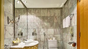 A bathroom with a marble-tiled wall, a white toilet, a sink with a yellow mosaic base, and a towel rack. - Hotel Prestige (Makkah)