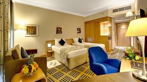 A hotel room with two beds, a sofa, a dining table, and a fruit bowl. - Hotel Prestige (Makkah)