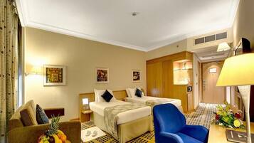 A hotel room with two beds, a sofa, a dining table, and a fruit bowl.
