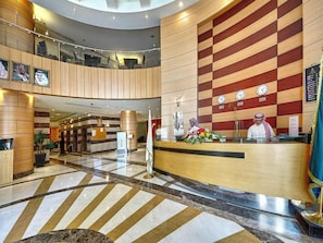 Un hall d’hôtel comprenant un comptoir d’accueil, un guichet d’enregistrement et un espace détente doté d’un plafond haut et d’un design moderne.