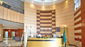 A hotel reception area with a curved wooden reception desk, a digital clock, and a flag.