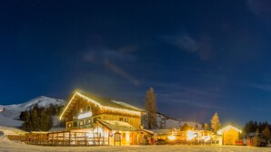 Un paysage de montagne enneigé, de nuit, avec un chalet illuminé et, au loin, un télésiège.
