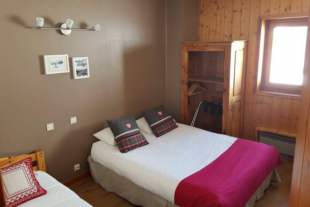 A bedroom with a bed, a wooden wardrobe, and a window.