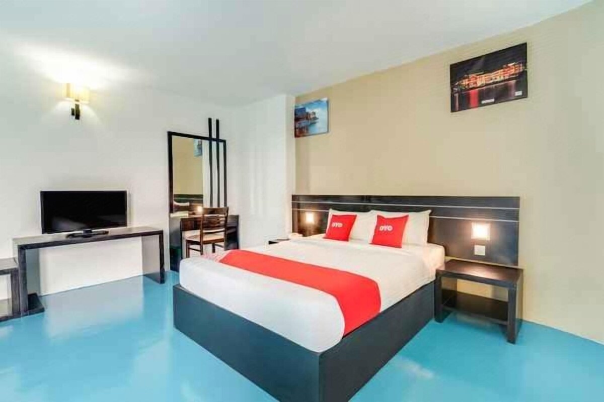 A hotel room with a bed, bedside tables, a desk, a television, and a mirror.