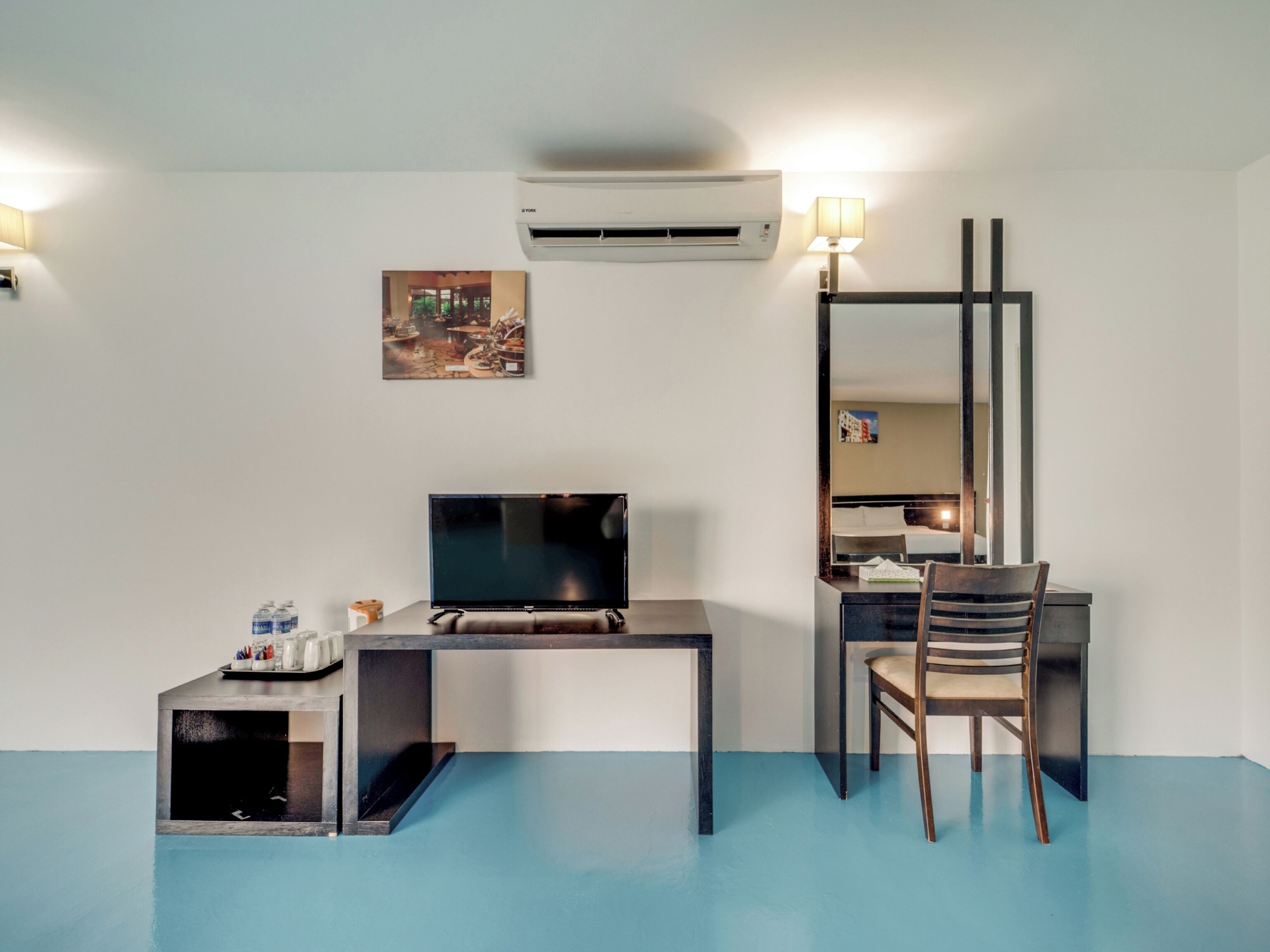 A hotel room with a desk, chair, flat-screen TV, air conditioning unit, and a mirror.