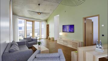 A modern living room with grey sofas, a wooden coffee table, a TV on the wall, and a wooden reception desk.