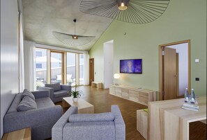 A modern living room with grey sofas, a wooden coffee table, a TV on the wall, and a wooden reception desk. - Green City Hotel Vauban (Freiburg im Breisgau)